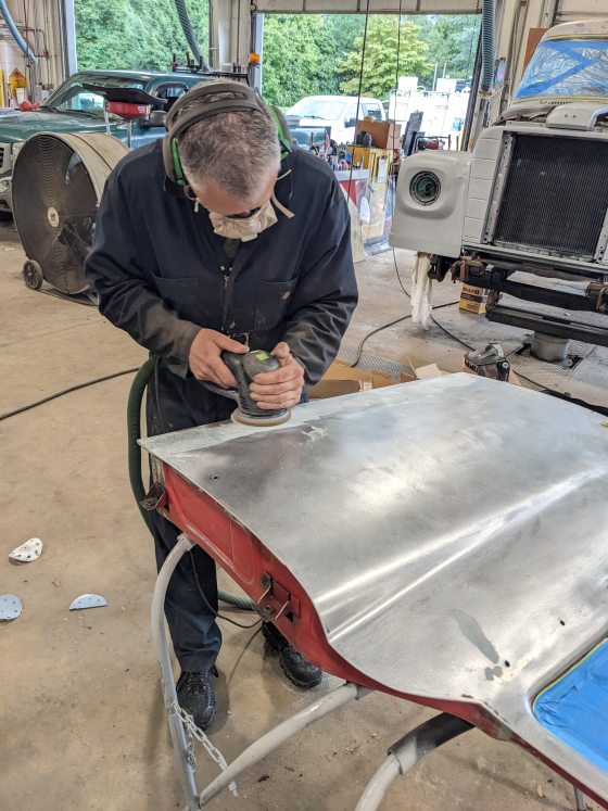 A person standing over a truck door sanding it down.
